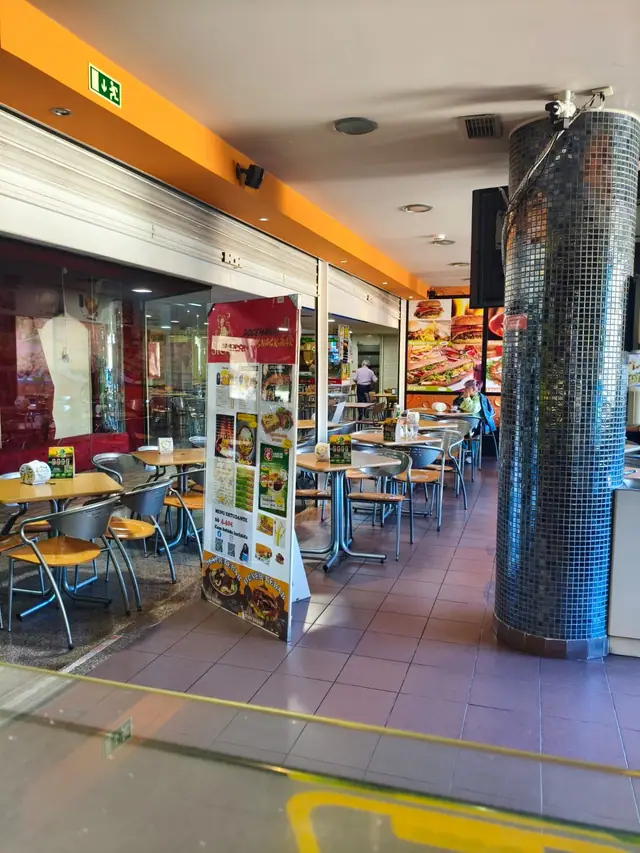 Mesas e cadeiras junto à Docemania no Centro Comercial D. Dinis, com o painel da ementa e uma coluna em mosaico azul
