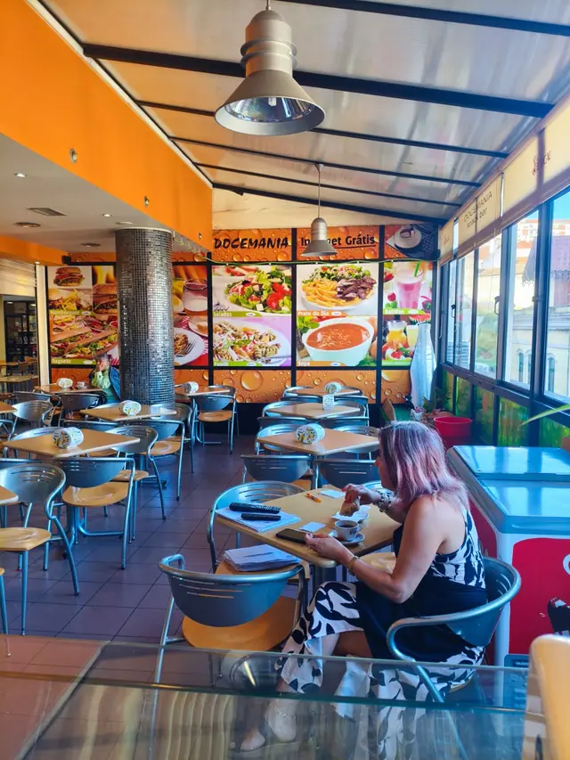 Sala da Docemania no D. Dinis com paredes laranja, painéis com saladas, prato do dia, sopa e batidos, e janelas com luz natural