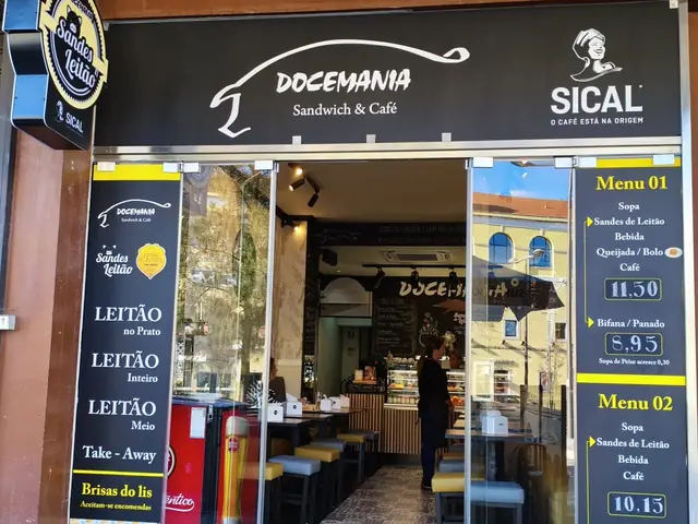 Entrada da Docemania no Centro Comercial Maringá, com o letreiro Docemania Sandwich & Café e os painéis da ementa e do leitão nas montras