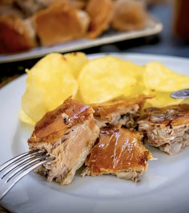 Garfo a pegar num pedaço de leitão, com batatas fritas no prato