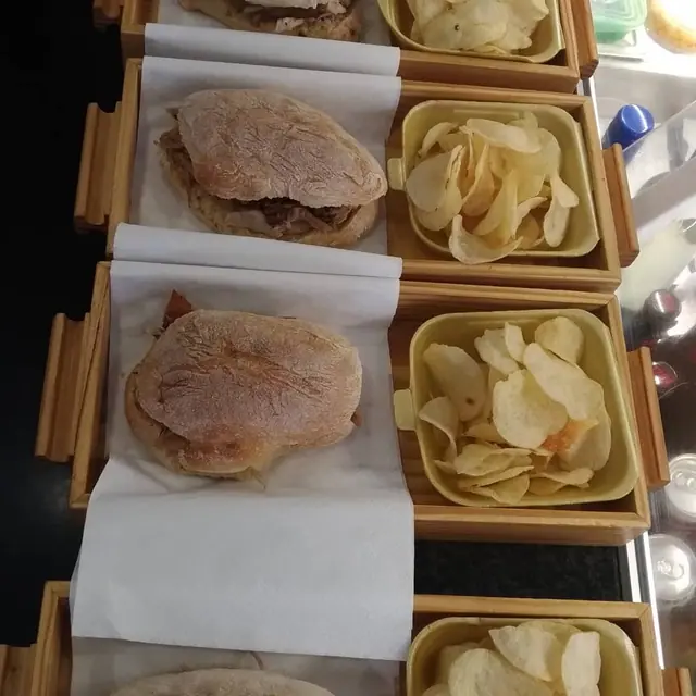 Várias caixas de madeira com sandes de leitão e batatas fritas, alinhadas no balcão